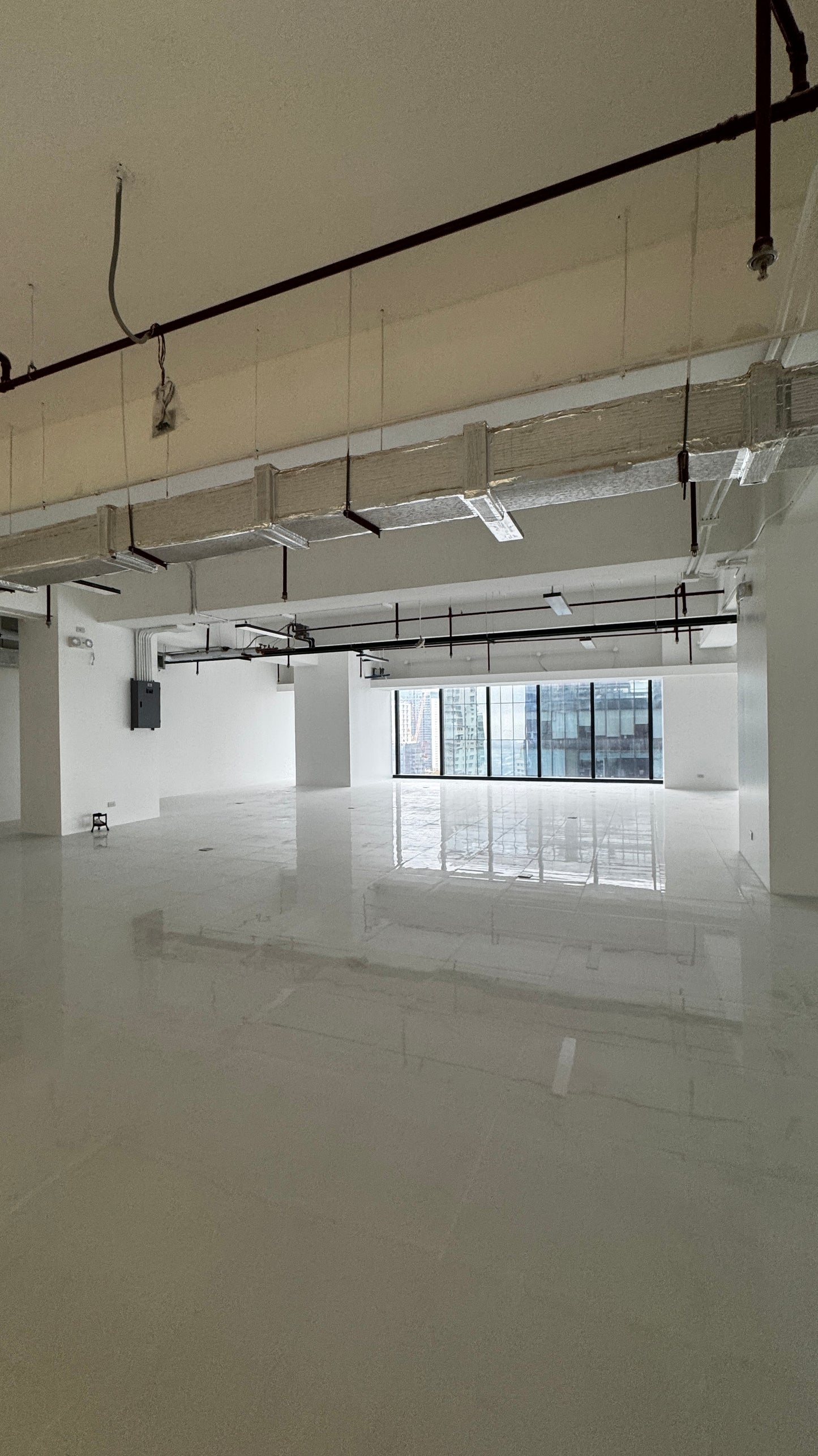 An empty, spacious industrial-style room with a polished light gray floor, white walls, and a high ceiling with exposed ductwork, pipes, and windows.